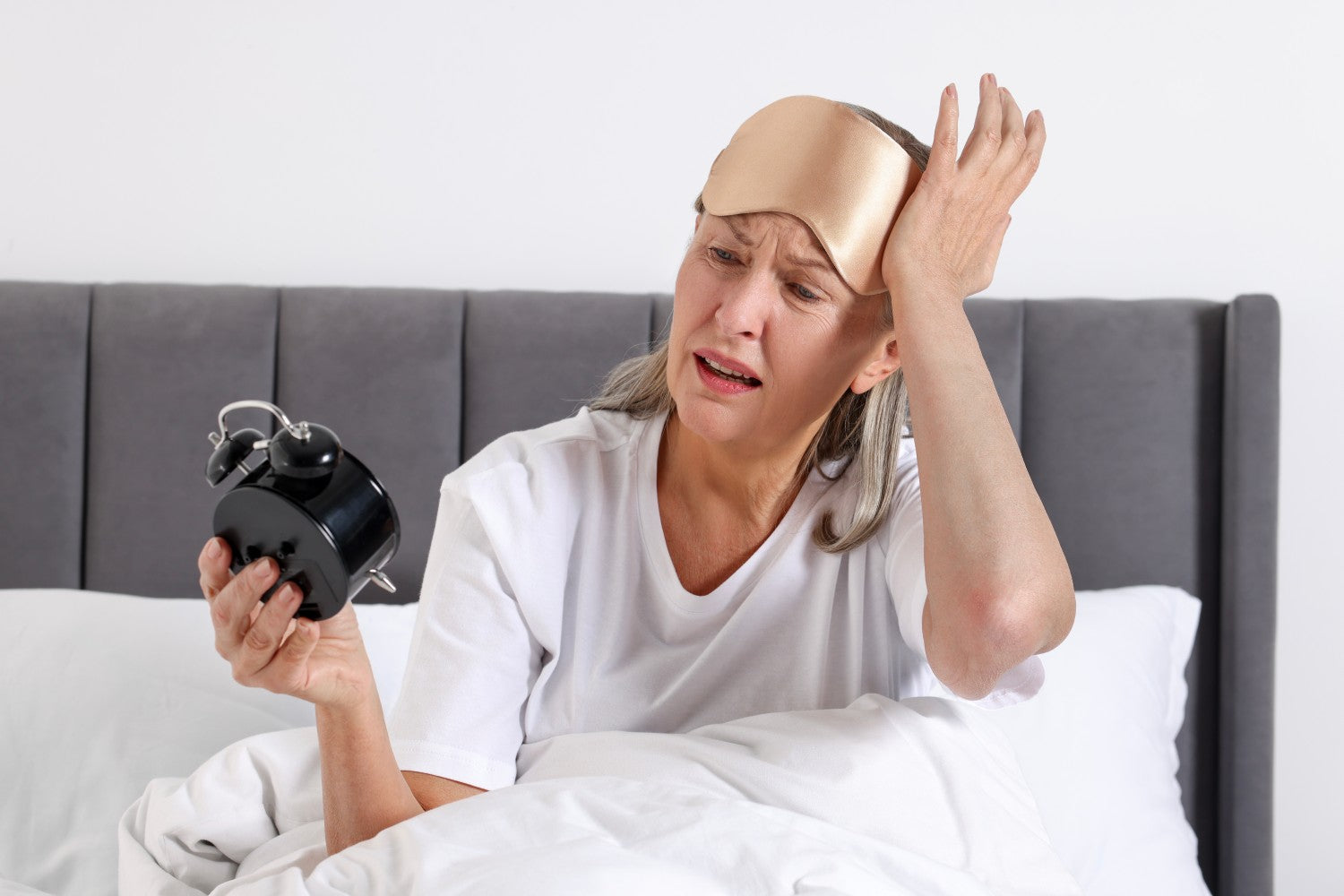 Eine Frau hält verschlafen einen Wecker in der Hand 