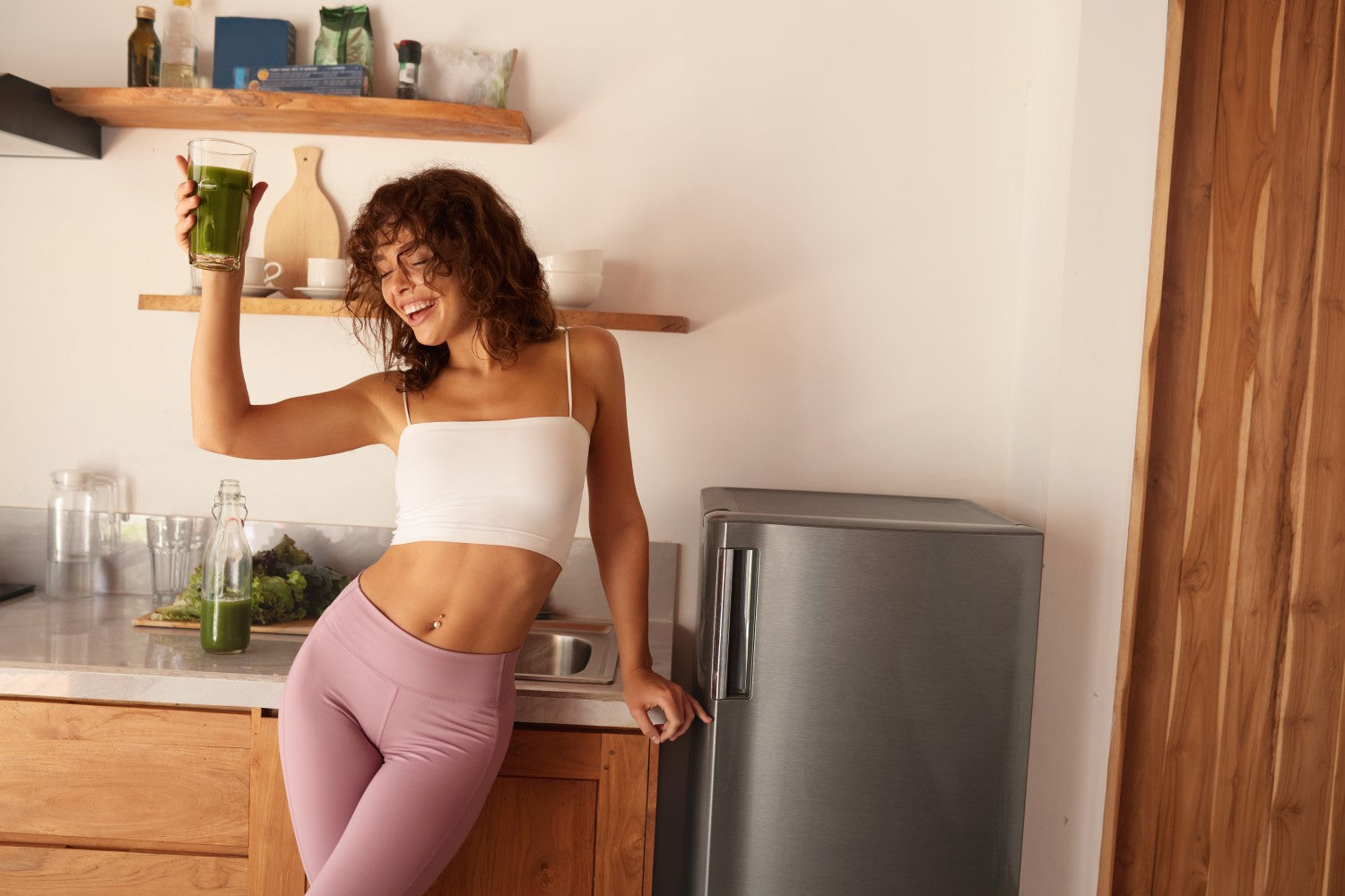 Eine lachende Frau hält einen grünen Smoothie in der Hand 