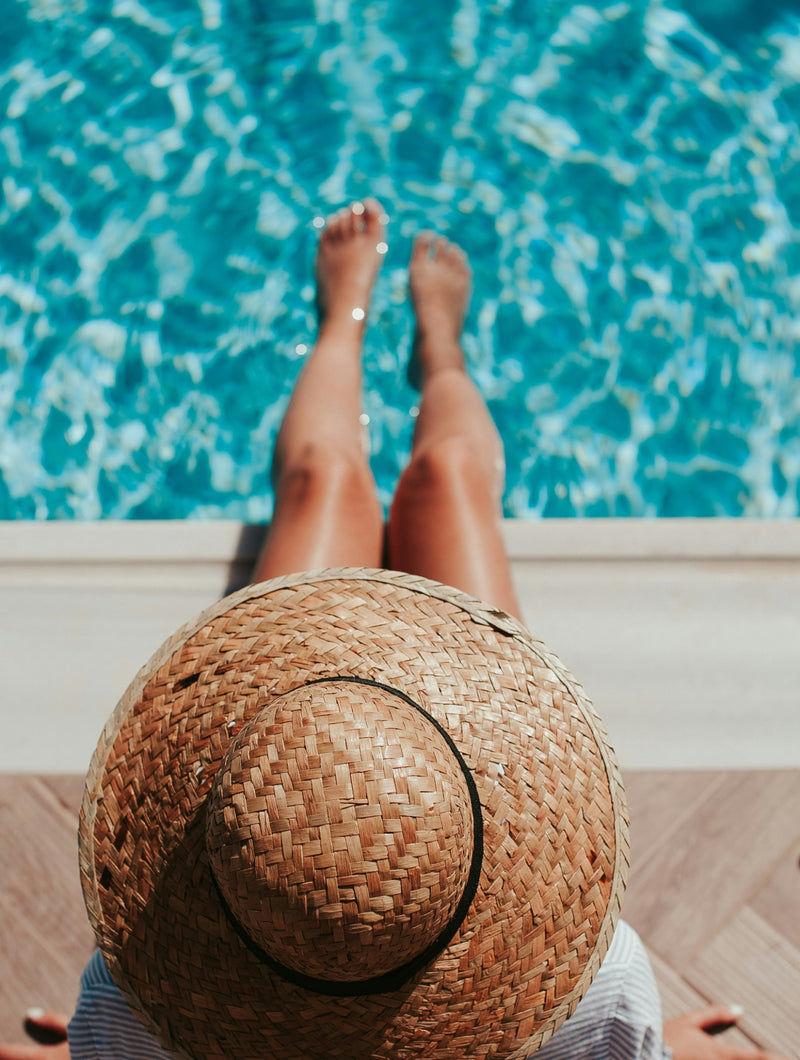 Frau sitzt bei Sonnenschein mit nackten Beinen entspannt am Poolrand .